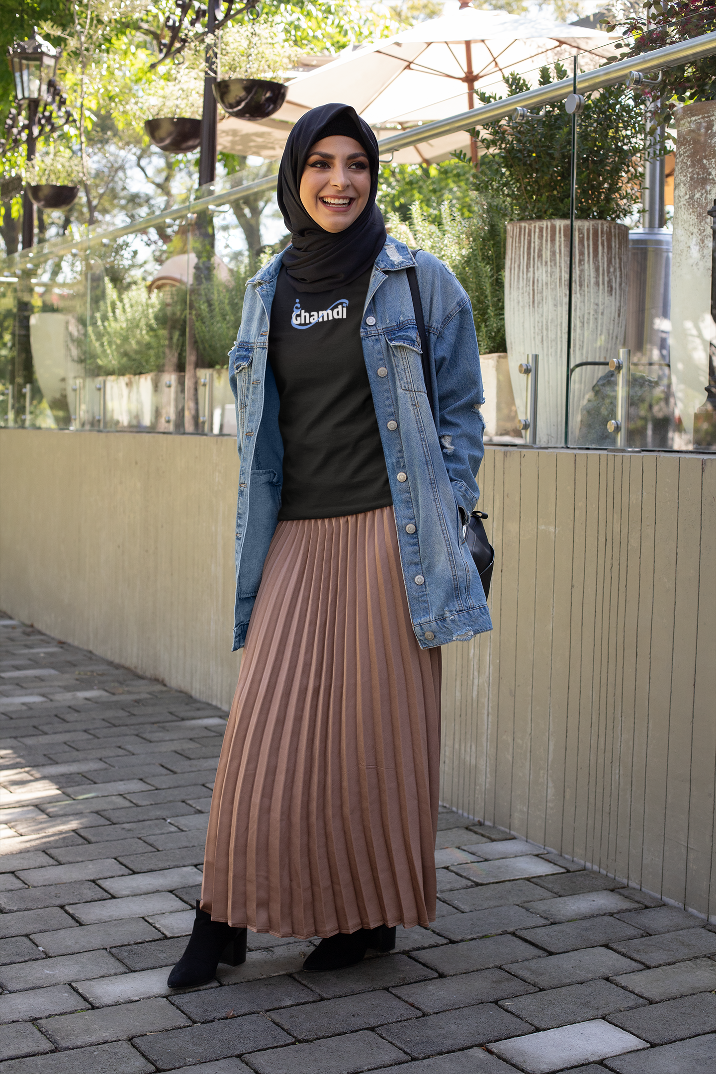 Woman wearing a denim jacket, black top, and pleated skirt standing outdoors.