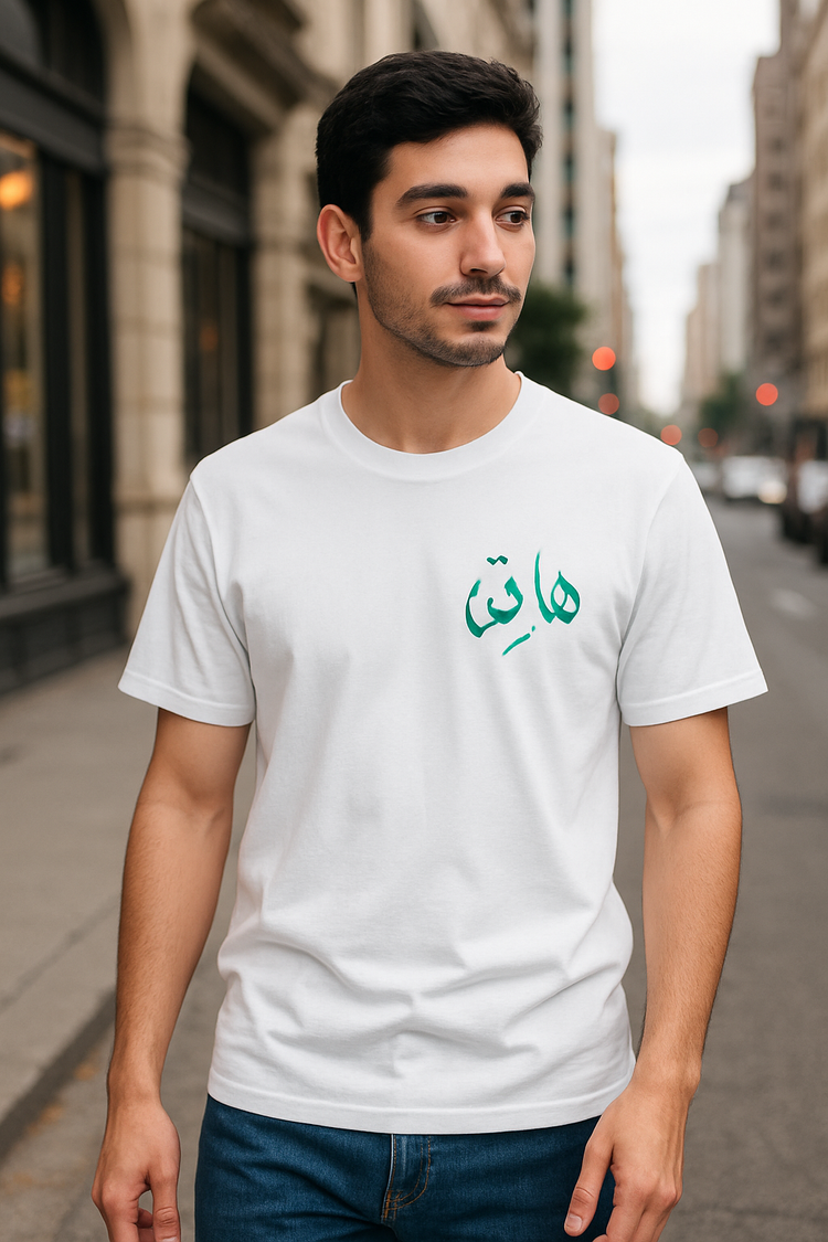 Man wearing a white t-shirt with green Arabic text on a city street