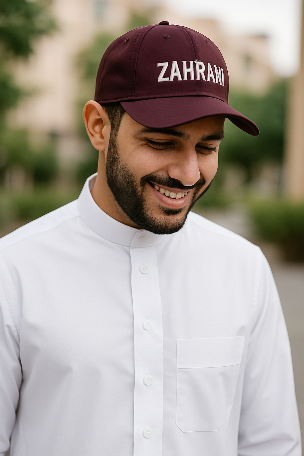 Man wearing a maroon cap with 'ZAHRANI' text, smiling outdoors.
